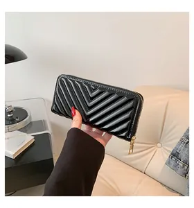 Handheld view of a black glossy V-quilted long wallet with golden zipper detail