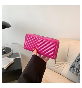Magenta glossy patent leather long wallet with V-pattern quilting held by a hand