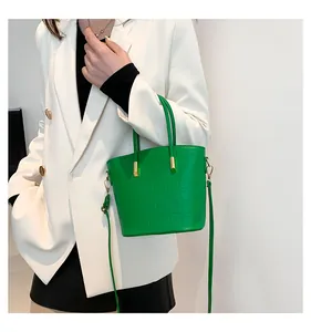 Detail of green crocodile embossed bucket bag featuring gold hardware on white blazer