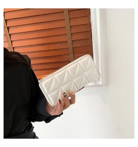 Détail d'une pochette beige matelassée géométrique avec fermeture éclair dorée et texture