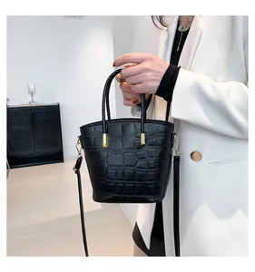 Close-up of black crocodile pattern bucket bag with gold hardware held by a model