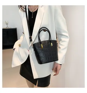 Detail of black crocodile pattern bucket bag styled with a white blazer for fashion