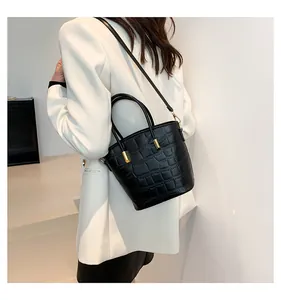 Detail of black crocodile texture bucket bag with gold hardware on white blazer