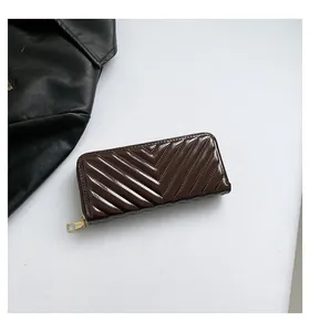 Macro detail of dark brown V-quilted glossy patent leather wallet with gold zipper hardware
