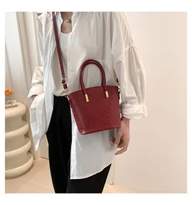 Close-up of red crocodile-patterned bucket bag with metallic handles worn by a model