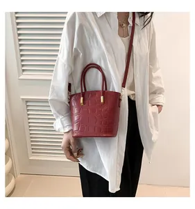 Model wearing a red crocodile pattern bucket bag with gold hardware and a shoulder strap