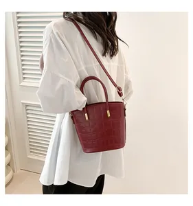 Detail of dark red crocodile embossed bucket bag with gold hardware and shoulder strap