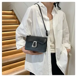 Close-up of a stylish black square crossbody bag with a matte silver buckle on leather