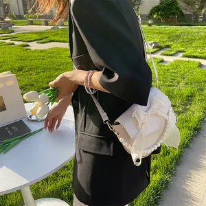 Close-up of cream bow shoulder bag with elegant pearl trim and sleek faux leather texture