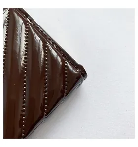 Detail shot of V-quilted dark brown patent leather wallet with silver bead embellishments