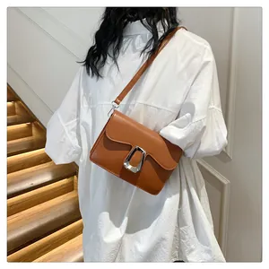 Detail of a brown flap crossbody bag with a silver U-shaped buckle on a white shirt