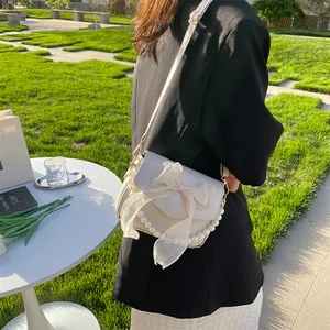 Detailed view of white leather bag with lace bow and pearl trim in an outdoor setting