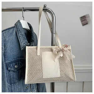 Detail of hollow-out straw tote bag featuring elegant lace bow and sleek faux leather panel