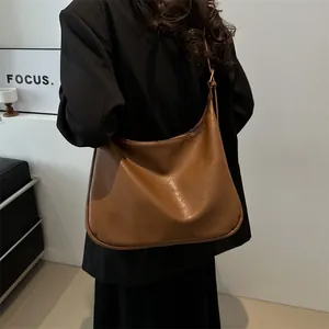 Große braune Leder-Hobo-Tasche mit verstellbarem Riemen am Modell vor weißem Hintergrund