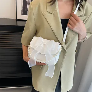 Detail of white leather handbag with lace bow and pearl chain worn on the shoulder