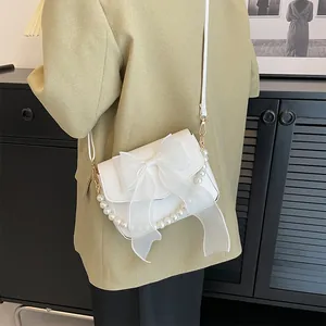 Detailed shot of white lace bow and pearl chain on stylish French square bag