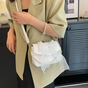 Close-up of white crossbody bag featuring large lace bow and elegant pearl chain detail