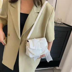 White lace bow crossbody bag with pearl chain shown on model in indoor lighting