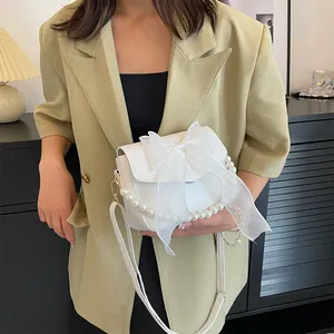 Close-up of elegant white lace bag with organza bow and pearl handle on a model