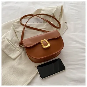 Close-up of caramel saddle bag with matte leather texture and gold geometric metal buckle