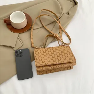 Brown printed crossbody handbag with M-letter pattern and adjustable strap on a neutral desk
