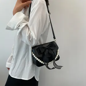 Detail of black lace bag with oversized silk bow and elegant white pearl chain strap