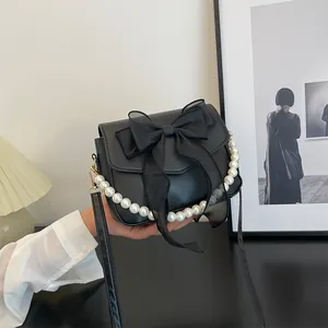 Detail of black leather bag featuring a large organza bow and elegant pearl chain