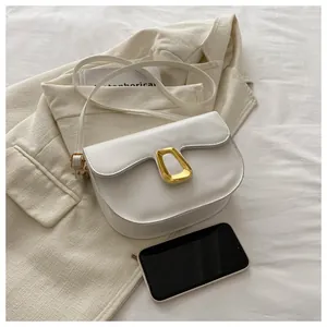 White leather saddle bag detail with gold geometric buckle next to a smartphone for size