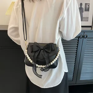 Detail of black bow bag with pearl chain strap and gold hardware on white shirt