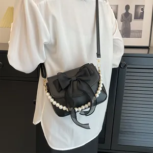 Detail of black faux leather bag with lace bow, pearl handle, and long strap