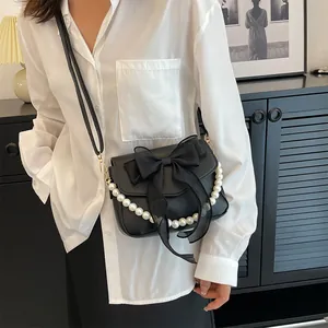 Close-up of black PU leather crossbody bag with oversized chiffon bow and pearl chain