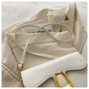 Close-up of white saddle bag with golden trapezoid buckle on a textured blazer background