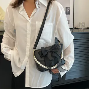 Detail of black bow and pearl chain on a stylish French lace textured crossbody bag