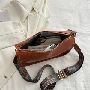Vintage brown leather cylinder bag with wide ethnic pattern strap and daily items inside