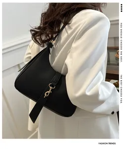 Detail einer schwarzen Leder-Achseltasche mit Goldschnalle auf weißem Blazer getragen
