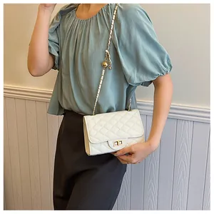 Detailed view of white quilted crossbody bag featuring golden chain and adjustable metal ball