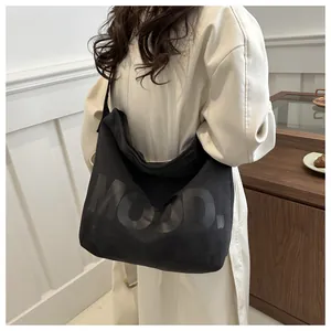 Detail of black canvas tote bag with MOOD lettering shown on a model in beige coat