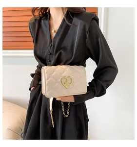 Détail du sac bandoulière matelassé avec boucle dorée en forme de cœur sur robe noire