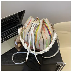 Detail of a beige knit bucket bag with colorful rainbow stripes and a plush monkey charm