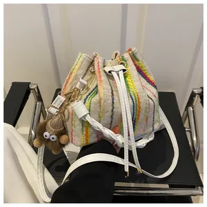 Close-up of cream canvas bucket bag with colorful stripes and brown plush doll charm