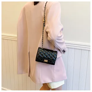Detail of classic black quilted bag with gold chain strap worn over a white suit