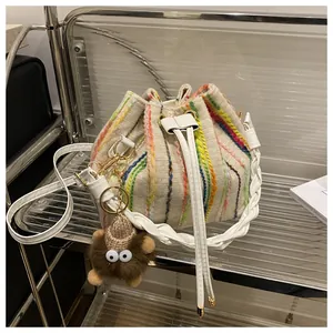 Detail of woven bucket bag featuring rainbow stripes and a brown plush monster charm