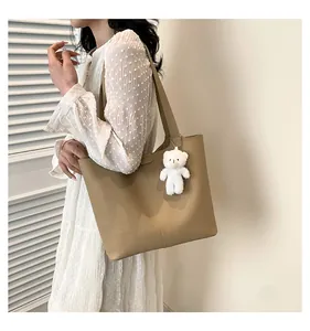 Detail of light brown lychee grain leather tote bag with cute plush bear charm