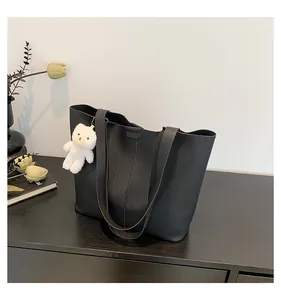 Detail of black lychee grain leather tote bag with a white bear plush charm on a table
