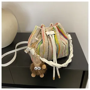 Detailed shot of beige canvas bucket bag with colorful vertical stripes and plush monster charm