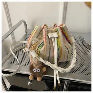 Detail of rainbow embroidered stripes and plush charm on a beige drawstring bucket bag
