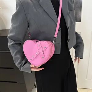 Sac à bandoulière rose en forme de cœur avec rivets argentés et lanières sur costume gris