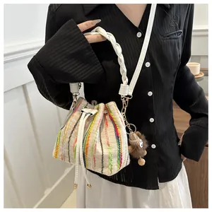 Close-up of a striped knit bucket bag featuring a drawstring closure and brown plush charm