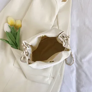 Elegant cream drawstring bucket bag with gold chain strap on soft fabric backdrop