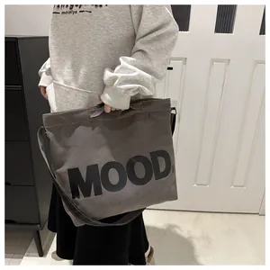 Close-up of the MOOD letter print on a large charcoal grey canvas crossbody bag